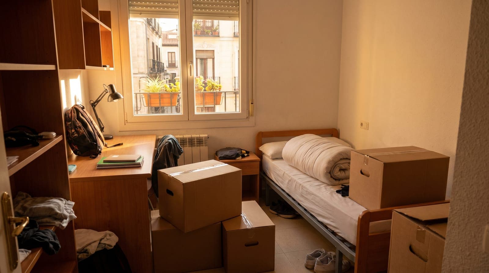 Habitación de estudiante en Madrid con cama, escritorio y cajas listas para la mudanza
